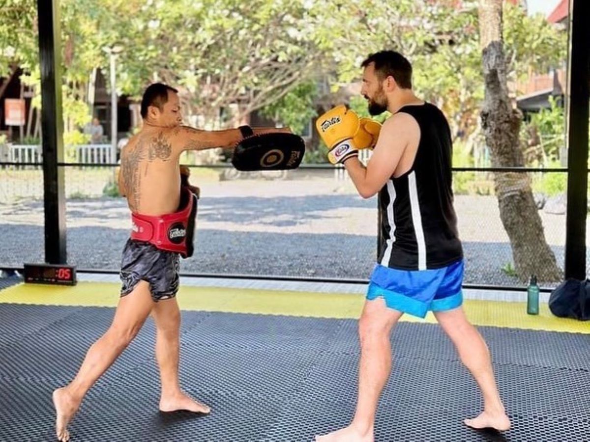 The trainer is guiding the pad toward the left side for practicing striking.